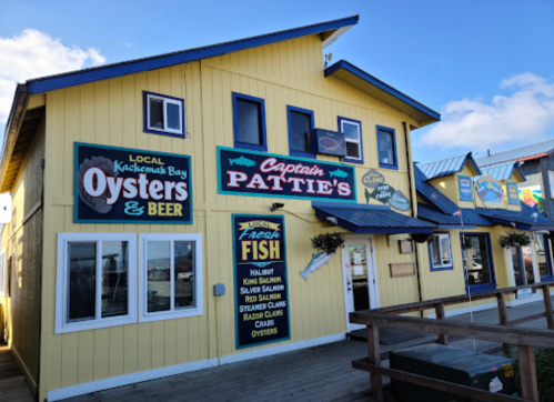 A yellow building with signs for Captain Pattie's, offering oysters, beer, and fresh fish, located by the water.