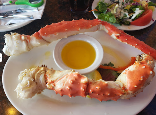 A large crab leg on a plate with a small bowl of melted butter and a side salad in the background.