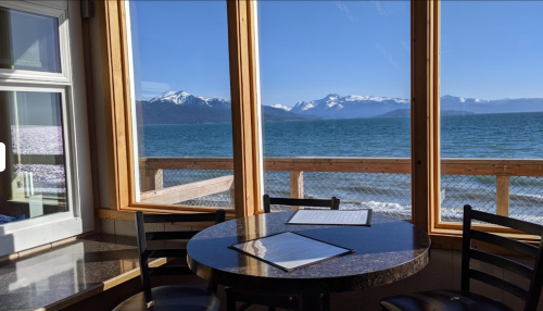 A cozy dining area with a round table and menus, overlooking a scenic view of mountains and a lake.