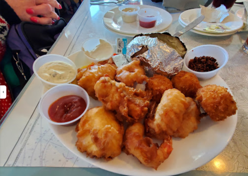 A plate of fried seafood, including shrimp and fish, served with various dipping sauces and a baked potato.