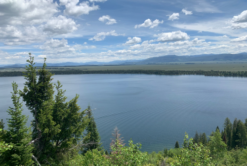 A serene lake surrounded by lush greenery and mountains under a partly cloudy sky.