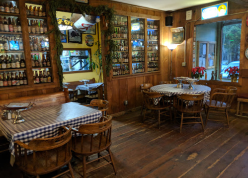 Cozy restaurant interior with wooden walls, checkered tablecloths, and shelves filled with bottles.