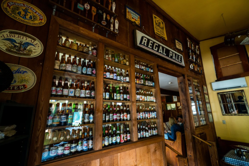 A wooden bar display filled with various beer bottles and vintage signs in a cozy pub setting.