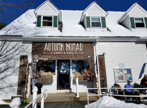 A cozy café named "Autumn Nomad" with a snowy exterior and decorative elements, inviting customers inside.