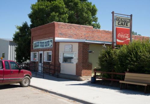 A brick building with a sign reading "Denton Cafe," featuring a Coca-Cola advertisement and a red truck parked nearby.