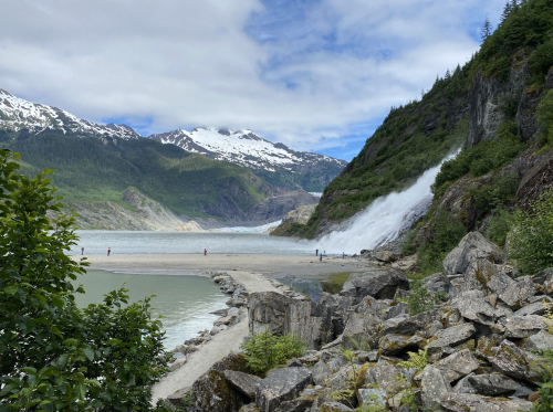 A scenic view of a waterfall cascading down rocky cliffs, surrounded by mountains and lush greenery.