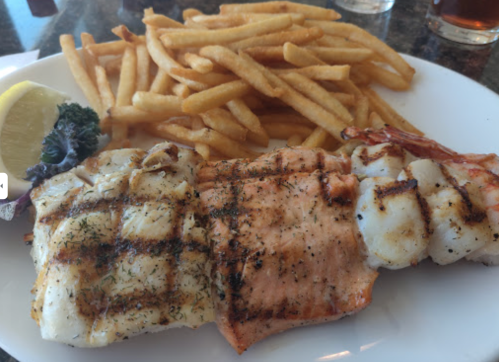 Grilled fish and shrimp skewer served with a side of crispy French fries and a lemon wedge.