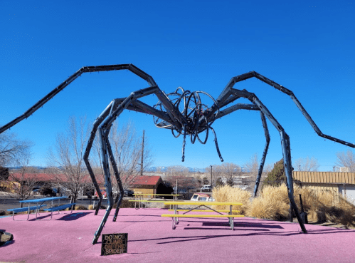 Giant metal spider sculpture on a pink surface, with a clear blue sky in the background.