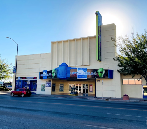 Exterior of a museum building with a blue and green sign, featuring alien-themed decorations and a bright sky.
