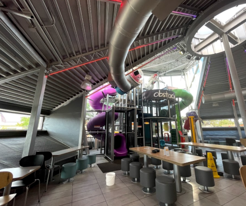 Interior of a modern play area featuring colorful slides, seating, and a bright, industrial design.