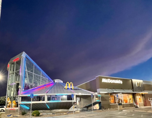 A modern McDonald's building with a unique triangular design, illuminated at night against a dark sky.