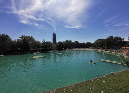 A serene lake with people enjoying water activities, surrounded by trees and a clear blue sky.