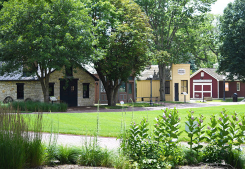A scenic view of a park featuring historic buildings and lush greenery on a sunny day.