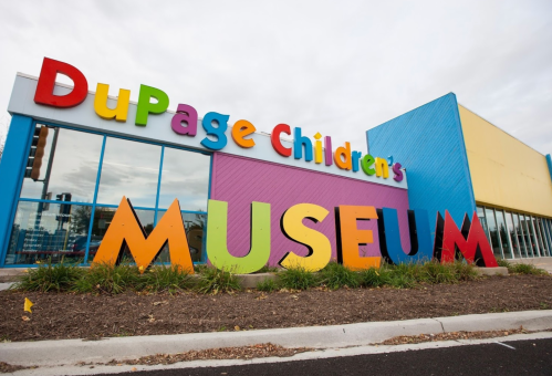 Colorful sign for DuPage Children's Museum, featuring large letters spelling "MUSEUM" in front of a vibrant building.