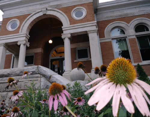 A close-up of pink and orange flowers in front of a historic brick building with a grand entrance.