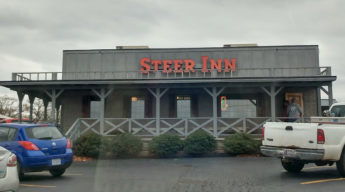 Exterior of a restaurant named "Steer Inn," featuring a wooden facade and parked cars in front.
