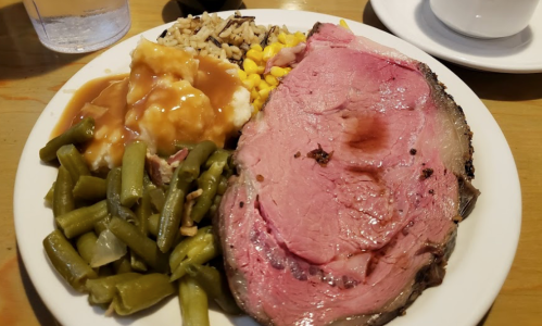 A plate of food featuring sliced roast beef, mashed potatoes with gravy, green beans, corn, and rice.
