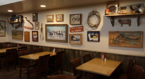 Cozy restaurant interior with wooden tables, chairs, and a wall adorned with various framed artworks and rustic decor.