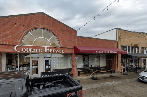 Exterior view of a brick building featuring "Courier-Herald" and "Cole Street Brewery" storefronts.