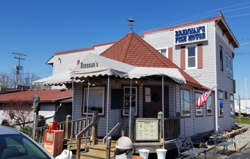 A quaint restaurant with a red-tiled roof, awning, and an American flag outside, surrounded by a scenic waterfront.