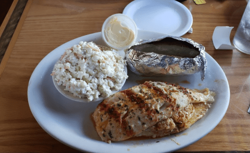 Grilled fish fillet with a side of coleslaw and a baked potato wrapped in foil on a white plate.