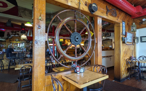 A rustic restaurant interior featuring wooden decor, a ship's wheel, and tables set for dining.