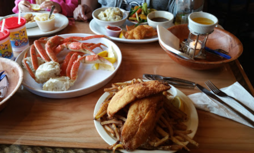 A table spread with seafood, including crab legs, fried fish, fries, and sides of mashed potatoes and vegetables.