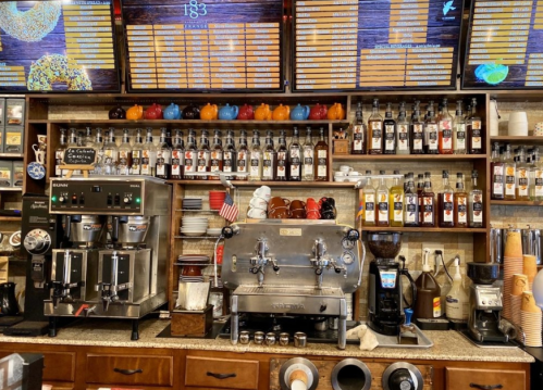 A coffee shop counter featuring espresso machines, syrups, and a menu displayed on screens above.