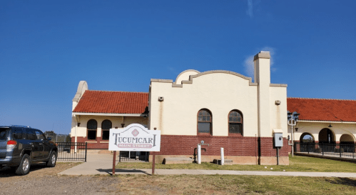 Historic Tucumcari train station with a red tile roof and a sign in front, set against a clear blue sky.