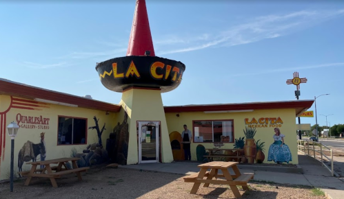 Colorful restaurant exterior with a large sombrero sign, featuring murals and outdoor seating.