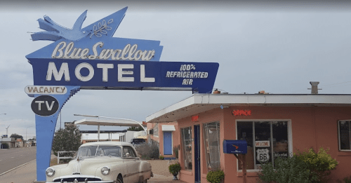 A vintage motel sign for Blue Swallow Motel with a classic car parked outside, located on Route 66.