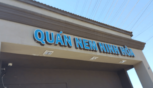 Sign for "Quán Nem Ninh Hòa" on a building exterior, with clear blue letters against a light-colored wall.