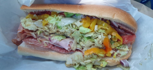 A large sub sandwich filled with layers of meats, lettuce, tomatoes, and colorful bell peppers.