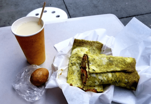 A plate with two rolled green wraps filled with eggs, an egg on the side, and a cup of white drink.
