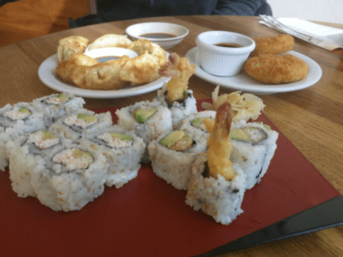 A table with sushi rolls, shrimp tempura, and dipping sauces in small bowls.