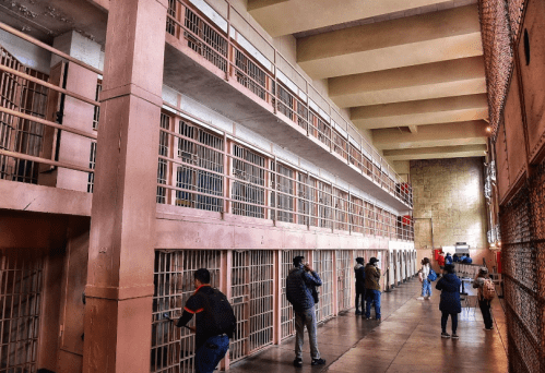 Interior of a prison with multiple levels of cells and visitors observing the surroundings.