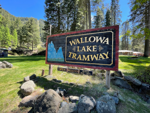 Sign for Wallowa Lake Tramway surrounded by trees and rocks, indicating it's open on weekends during the season.