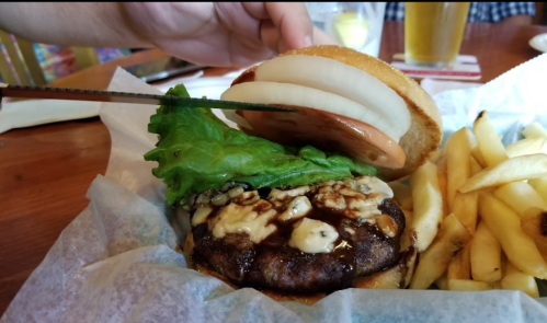 A close-up of a burger with lettuce, onion, and sauce, served with a side of fries on a wooden table.