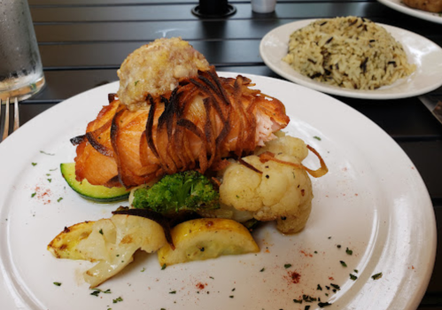A plate featuring salmon topped with crispy onions, served with grilled vegetables and a side of rice.