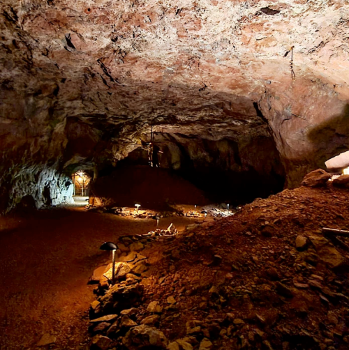 A dimly lit cave interior with rocky walls, scattered lights, and a dirt floor, creating an atmospheric underground scene.