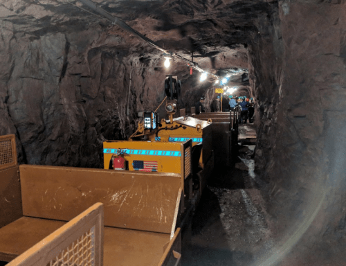 A dimly lit mine tunnel with mining carts lined up on a track, surrounded by rocky walls.