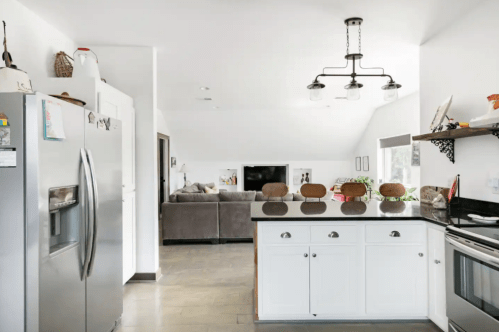 Modern kitchen with stainless steel appliances, a black countertop, and a cozy living area in the background.