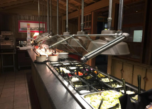 A buffet station with various food items under glass covers, featuring salads and toppings in organized trays.
