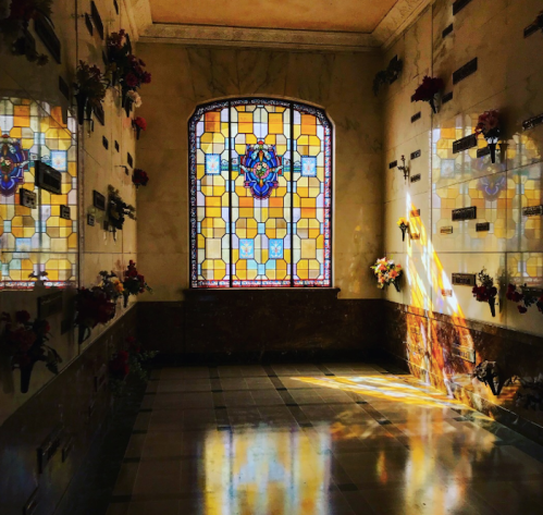 A serene interior of a mausoleum with stained glass windows and soft light illuminating the space.
