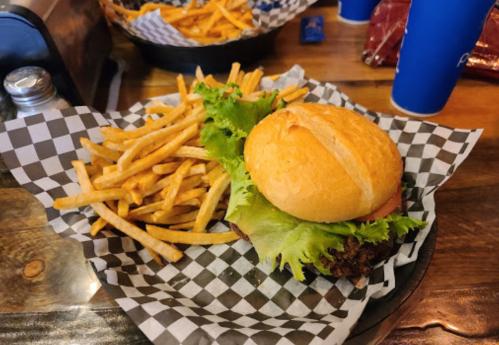 A burger with lettuce and tomato on a checkered plate, accompanied by a side of golden fries.