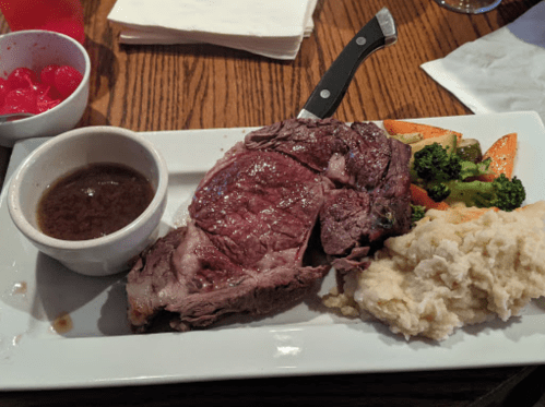 A plate featuring a large slice of roast beef, gravy, mashed potatoes, and mixed vegetables.
