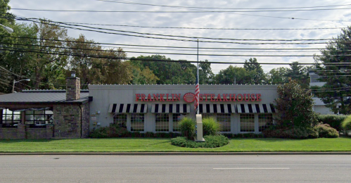 Exterior view of Franklin Steakhouse, featuring a stone facade and large windows, with an American flag in front.
