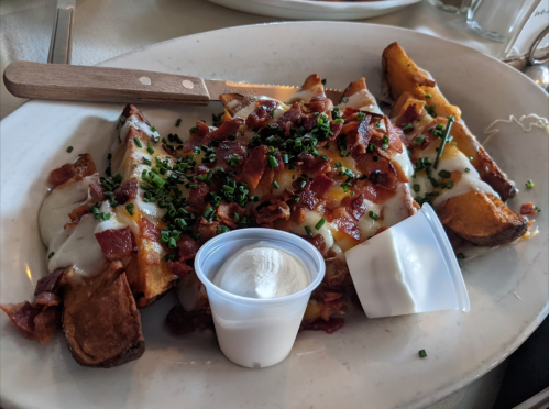A plate of loaded potato wedges topped with cheese, bacon, and chives, served with a side of sour cream.