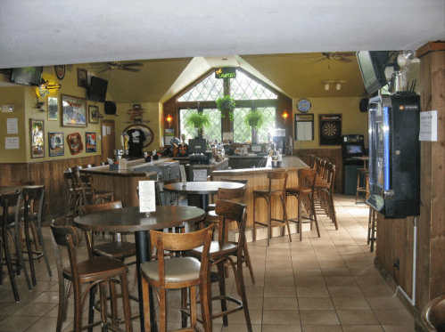 Interior of a bar with wooden tables, chairs, a bar counter, and dartboard, featuring a cozy, inviting atmosphere.