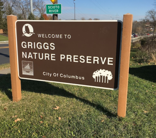 Sign welcoming visitors to Griggs Nature Preserve, located in the City of Columbus, with a Scioto River sign in the background.